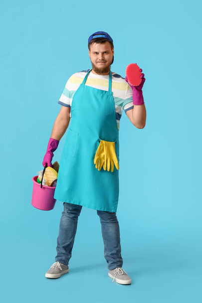 Young man with cleaning supplies on blue background - Photo, image