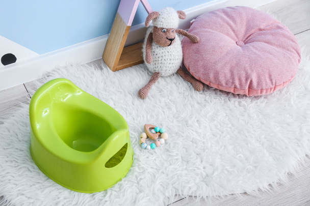 Green potty, toy sheep and pillow on floor - Фото, изображение