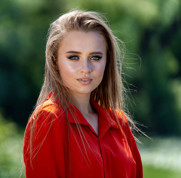 Portrait of the beautiful sexy woman with long blonde hair. Fashion young girl in red dress posing in nature on a river background with flying hair - Fotografie, Obrázek