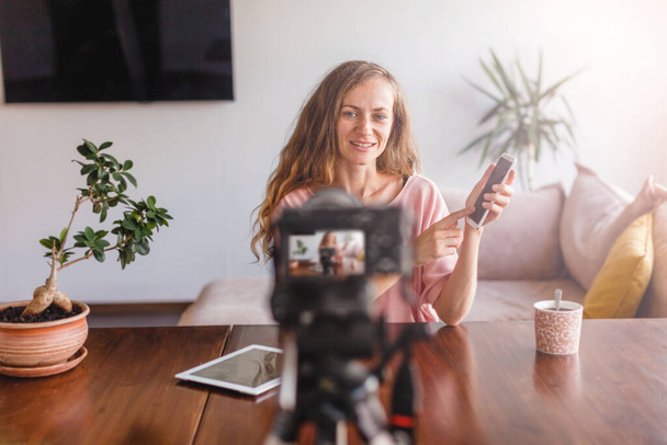 Young attractive happy woman blogger or vlogger looking at camera and talking on video shooting with technology. Social media influencer people or content maker concept in relax casual style at home - Foto, Bild