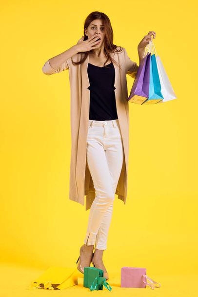 smiling woman with multicolored bags posing yellow background - Foto, Imagem