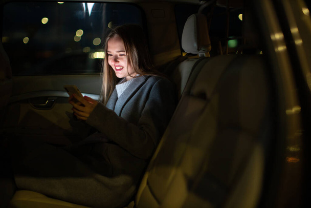 Young woman with her cell phone sitting in the backseat of a car, getting ready to travel (color toned image; shallow DOF) - Foto, imagen