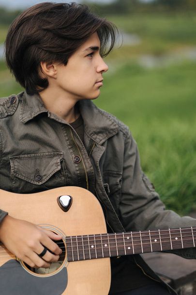 Portrait of handsome teenage boy playing guitar outdoor. Boy using classic guitar. Male alone making music - Photo, Image