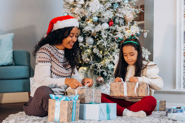 Mom and daughter sit on carpet opening Christmas presents - Foto, Imagem