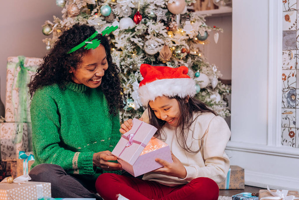 Tochter und Mutter in Weihnachtsmützen öffnen Geschenke - Foto, Bild