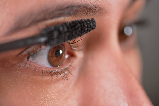 Close-up macro of young Latina woman wearing eyelash mascara at home. - Foto, Imagem