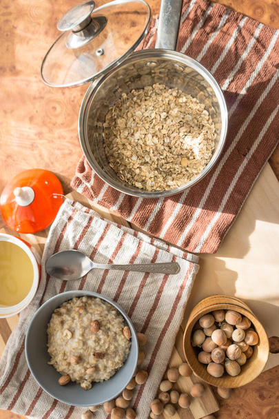 Gesunde, diätetische und nahrhafte Haferflocken mit köstlichem hausgemachten Honig, Haselnüssen in einem grauen Teller auf der Tischplatte Ansicht. - Foto, Bild