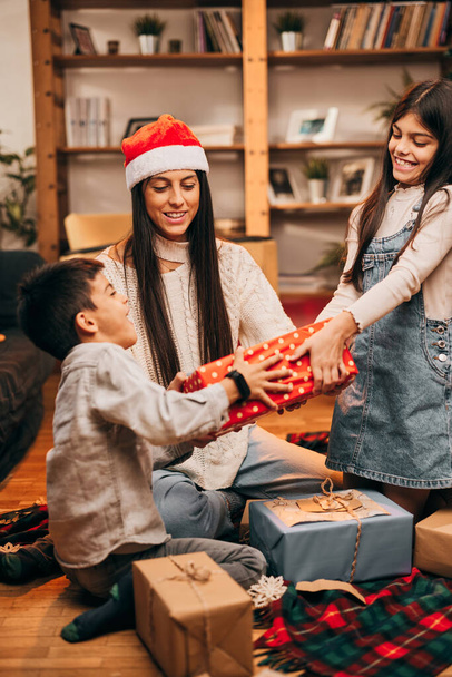 Dzieci walczą o prezenty, podczas gdy ich matka usiłuje rozwiązywać kłótnie w świątecznym duchu.. - Zdjęcie, obraz