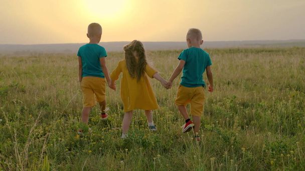 Kinder, Jungen, ein Mädchen laufen händchenhaltend über das Feld. Kindheitsfreunde reisen in die Natur, Kindheitsträume. Eine Gruppe von Kindern spielt gemeinsam im Park. Kindheitsfreundschaftskonzept - Foto, Bild