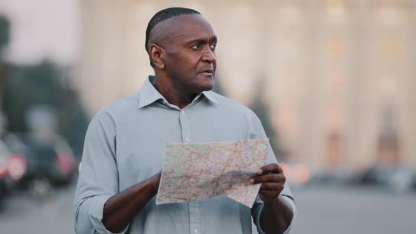 Volwassen volwassen zwarte buitenlandse toerist op zoek naar adres verloren Afro-Amerikaanse man reiziger in nieuwe stad staan op straat buiten met kaart zoeken weg bestemming navigatie route rond te kijken - Video