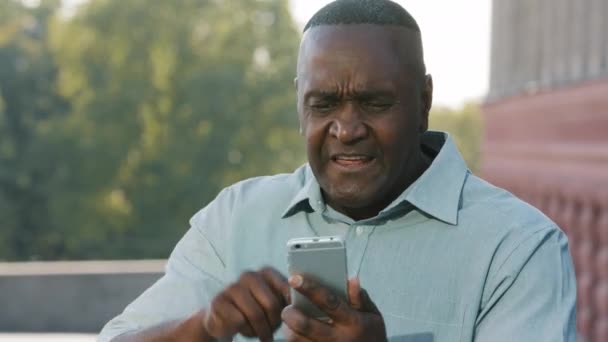 Mad τόνισε αφρικανός άνδρας κρατώντας κινητό τηλέφωνο ενοχλημένος με το μήνυμα spam λάθους εφαρμογή για κινητά σε αργό κολλήσει σπασμένο smartphone, θυμωμένος μαύρο άτομο απογοητευμένοι από το πρόβλημα του τηλεφώνου έχουν παράπονα για την κακή εξυπηρέτηση - Πλάνα, βίντεο
