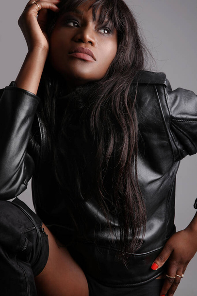 Gorgeous black young woman with long hair wears black leather jacket. Vertical. - Fotó, kép