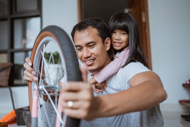 Hija sonríe y abraza a su padre mientras arregla una rueda - Foto, imagen