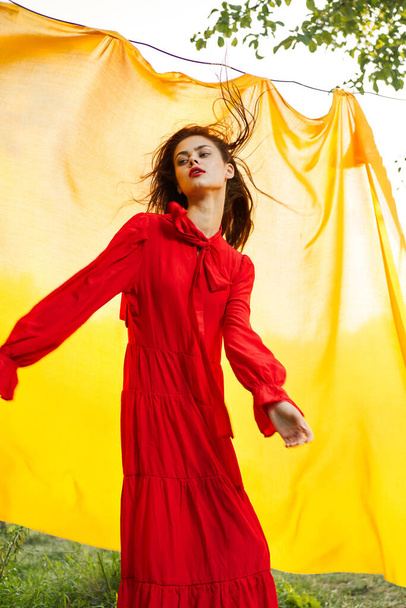 pretty woman in red dress yellow fabric on nature background - 写真・画像