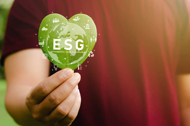 Green Energy ESG Erneuerbare und nachhaltige Ressourcen im Umweltschutz und in der Ökologie Großaufnahme eines jungen Mannes, der ein herzförmiges grünes Blatt in die Kamera hält - Foto, Bild