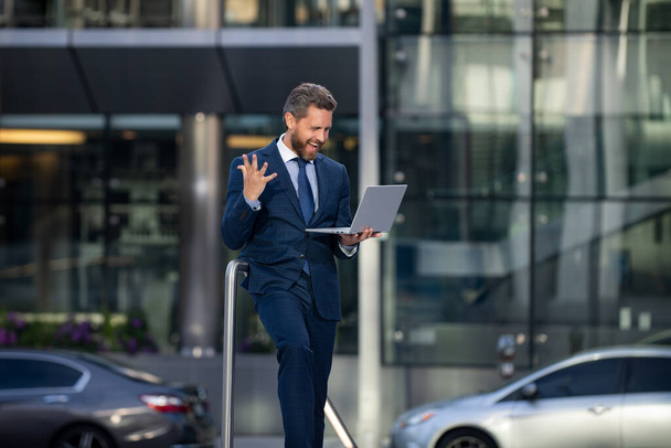 Portrait of excited businessman using laptop outdoor. - Фото, изображение