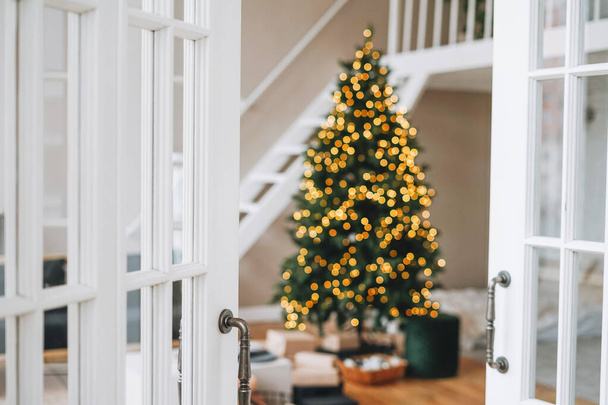 Θολή Διακοσμημένο χριστουγεννιάτικο δέντρο με κουτιά δώρων από λευκή πόρτα στο φωτεινό εσωτερικό στο σπίτι - Φωτογραφία, εικόνα