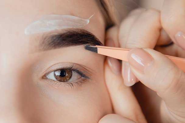 Master wax depilation of eyebrow hair in women, brow correction with tweezers - Photo, image