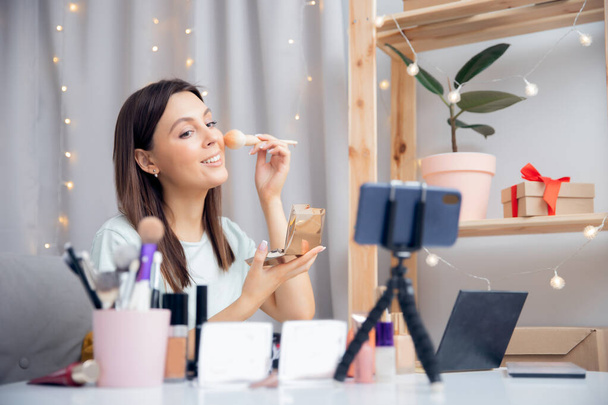 Concept Influencer blogger beauty blog. Happy woman vlogger is showing cosmetics products while recording video stream on phone - Photo, image