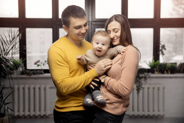 Happy family kiss small baby son on background of window, sunlight - Photo, Image