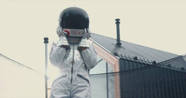 Happy childhood dreams. Kid in white space suit, helmet jumps on sunny trampoline having fun outside playing astronaut. - Zdjęcie, obraz