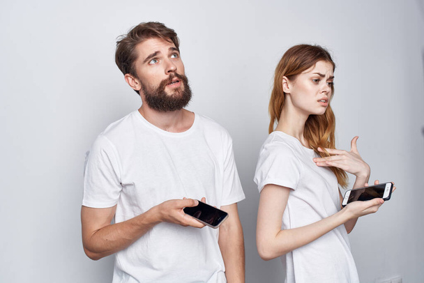 una joven pareja de camisetas blancas con teléfonos en las manos fondo claro - Foto, Imagen