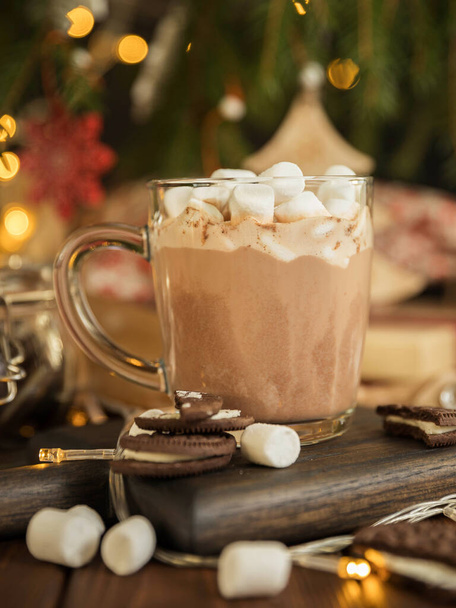 Heiße Schokolade mit Marshmallow in einer Glasschale auf einem Holztisch unter dem Weihnachtsbaum. Heißgetränk und Weihnachtsbaum. Weihnachtsgrußkarte. - Foto, Bild