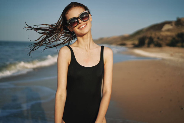 woman walks along the sandy shore in a black swimsuit sun tropics - Foto, afbeelding