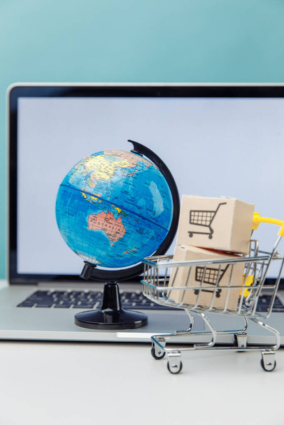 Online nakupování a ekommerce koncept. Nákupní košík Globe a supermarket s krabicemi u notebooku. Svislý obrázek - Fotografie, Obrázek
