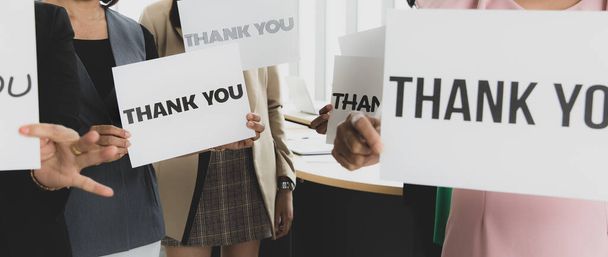 Group of businesspeople join together greeting and hold thank you word for sign of thankfulness to someone in modern office. Idea for good teamwork feeling declaration and support for colleagues. - Photo, image