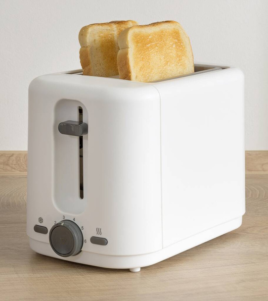 Tahta mutfak çalışma masasında elektrikli tost makinesinde iki dilim altın kahverengi tost. - Fotoğraf, Görsel