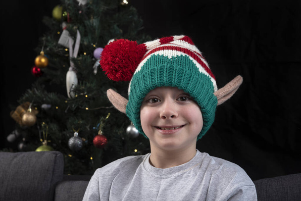 Портрет хлопчика в різдвяному ельфійському капелюсі на фоні ялинки
. - Фото, зображення
