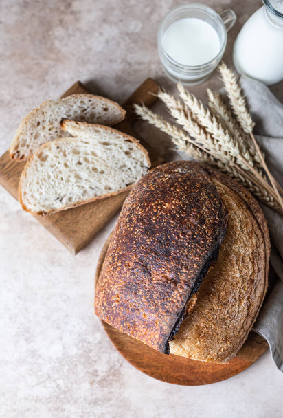 Loaf of freshly baked sourdough bread on cutting board with milk. Artisan rustic sourdough bread. Top view. - Foto, Bild