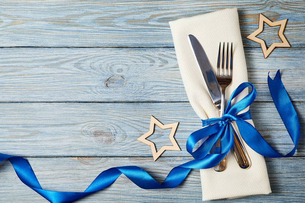 Knife and fork on napkin tied with blue ribbon on wooden background decorated with stars - Photo, image