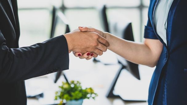 Close-up handshake of two businesspeople in modern office. Businessman and businesswoman shake hand with computer background. Concept of a business partner, business meeting, and collaboration - Photo, Image