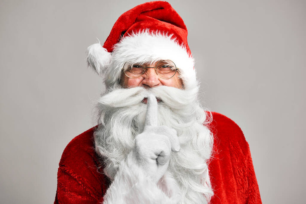 Santa Claus standing on the grey background and showing quiet sign  - Fotografie, Obrázek