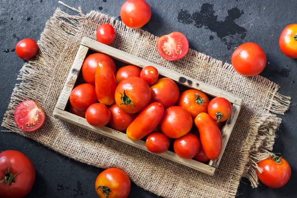 Fresh red tomatoes in wooden box on black background. Flat lay, top view - Φωτογραφία, εικόνα