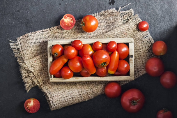 Fresh red tomatoes in wooden box on black background. Flat lay, top view - Φωτογραφία, εικόνα