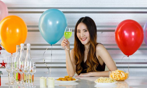 Menina bonita asiática em vestido sexy sentado sorrindo olhar para a câmera segurando coquetel de martini de maçã verde em brindes de vidro de vinho alto e brindar em festa no bar de lanches do balcão de alimentos e bebidas. - Foto, Imagem