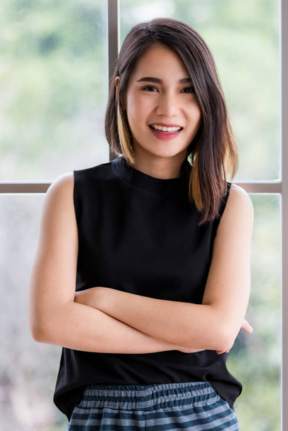 Portrait shot of a cute smiling Asian woman with a stylish straight hairstyle in black clothes standing and looking at the camera with crossed arms posing in the studio. - Foto, Imagen