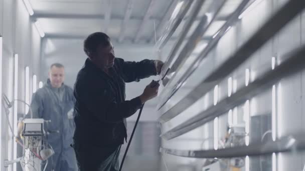 Twee mannen aan het werk in de verfwinkel. Molaire werkplaats en werknemer verwerkt stalen profielen van stof en deeltjes alvorens in slow motion te schilderen - Video