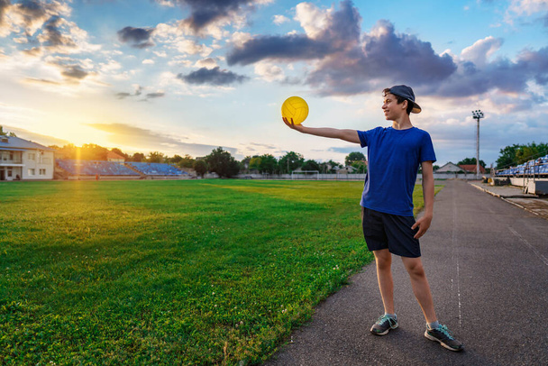 tini fiú pózol labdát a stadionban, ő tartja a labdát a kezében, egy focipálya zöld fű - sport és egészségügyi koncepció - Fotó, kép