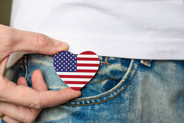 Patriot of the USA! Wooden badge with USA flag in the shape of a heart in a man's hand. - Foto, Bild