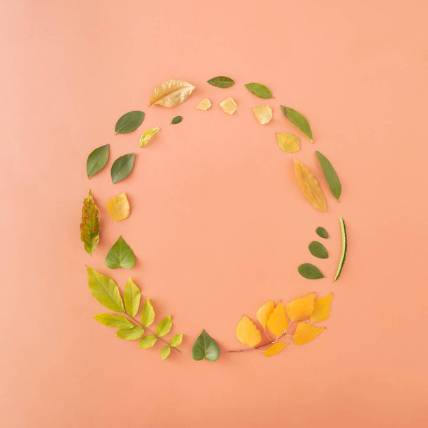 Circle of green, yellow, golden and brown autmn leaves on sandy pastel background. Creative representation of seasonal change. Flat lay composition. - Photo, Image