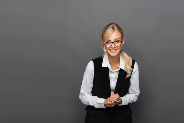 Positive businesswoman in eyeglasses looking at camera isolated on grey  - Fotó, kép