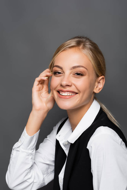 Cheerful blonde businesswoman looking at camera on grey background - Photo, Image