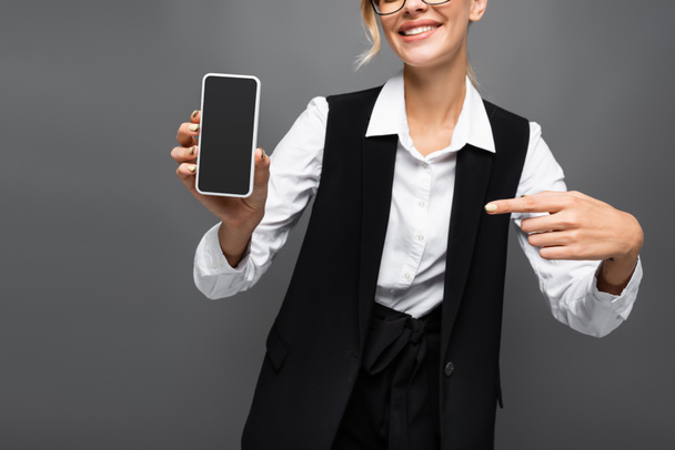 Gevoelige weergave van glimlachende zakenvrouw wijzen met de vinger naar smartphone geïsoleerd op grijs  - Foto, afbeelding