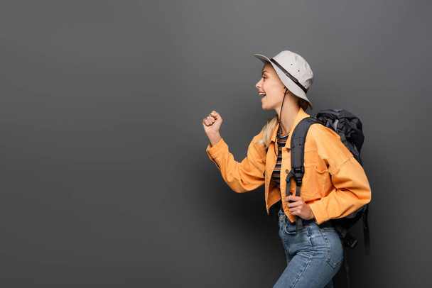 Side view of cheerful traveler with backpack showing yes gesture on grey background - Fotoğraf, Görsel