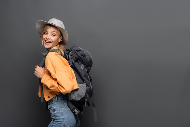 Positive tourist with backpack and hat looking away isolated on grey  - Foto, Imagem