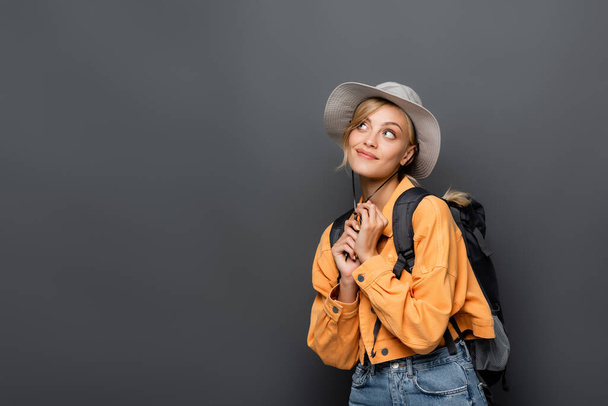 Dreamy traveler with backpack looking away isolated on grey  - Photo, Image